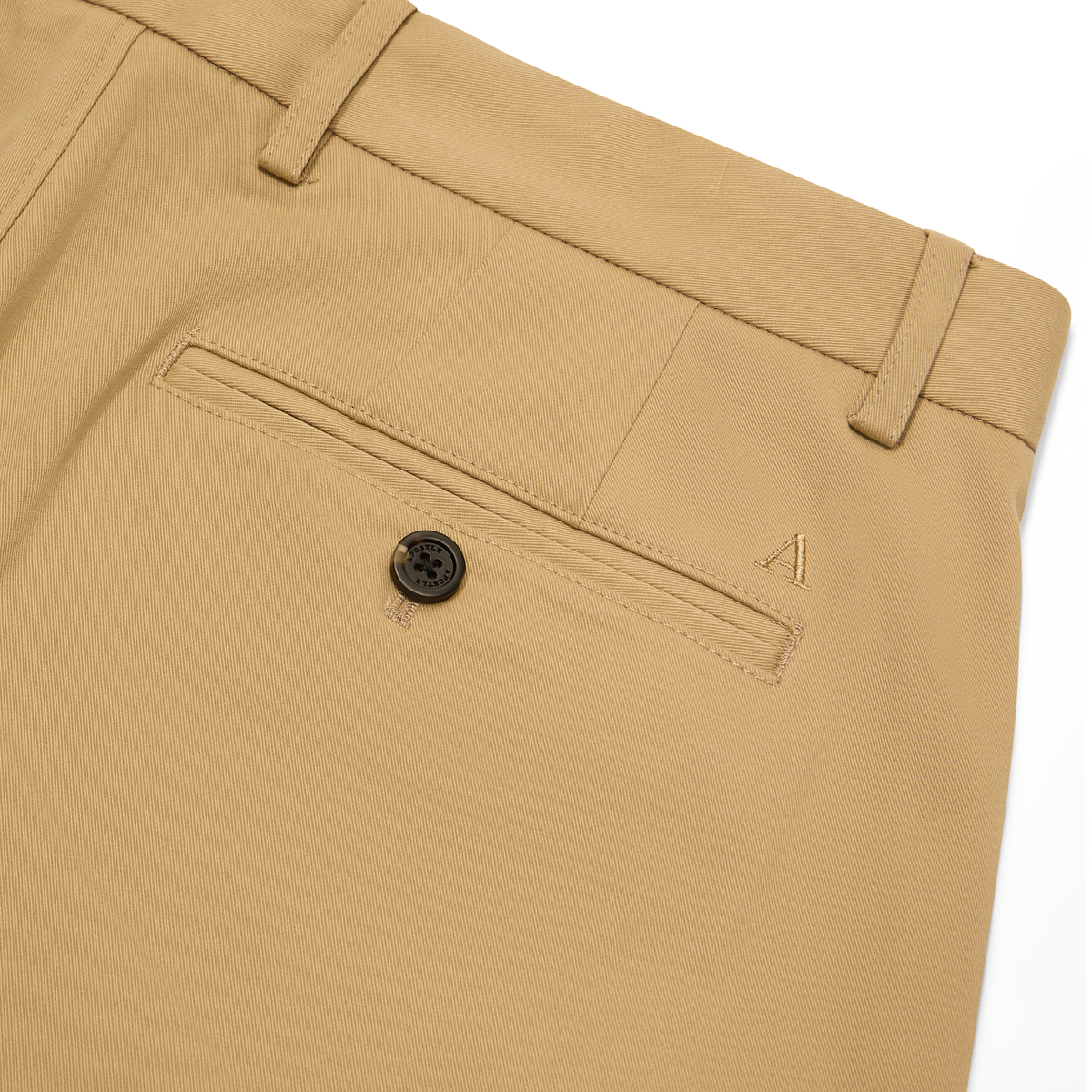 Close-up of tan chinos showing the back pocket with a black button and a small embroidered logo on the side, on a white background.